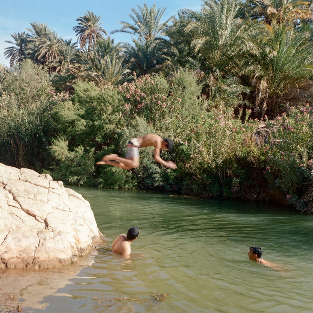 Three young boys jumping in and swimming around the water in an oasis.